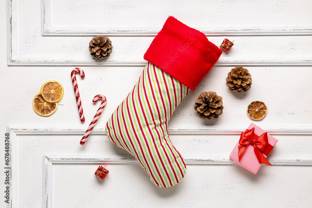 Christmas sock with candy canes, cones, dried orange and gift box on white background