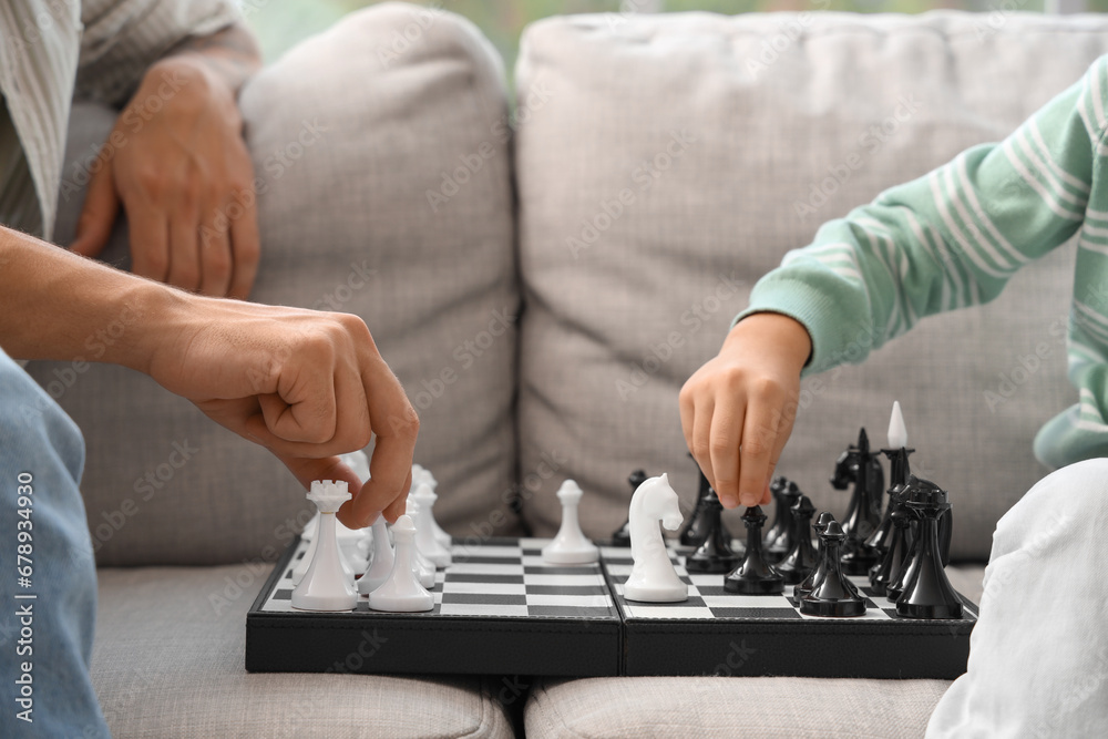 Young man with his little son playing chess at home, closeup