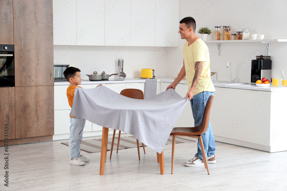 Young man with his little son setting dining table in kitchen