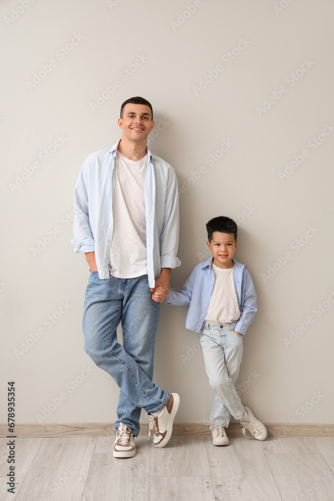 Young man with his little son holding hands near light wall