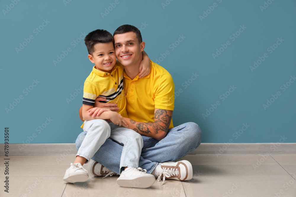 Young man with his little son hugging near blue wall