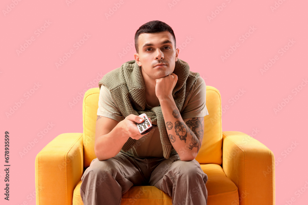 Young man in armchair watching TV on pink background