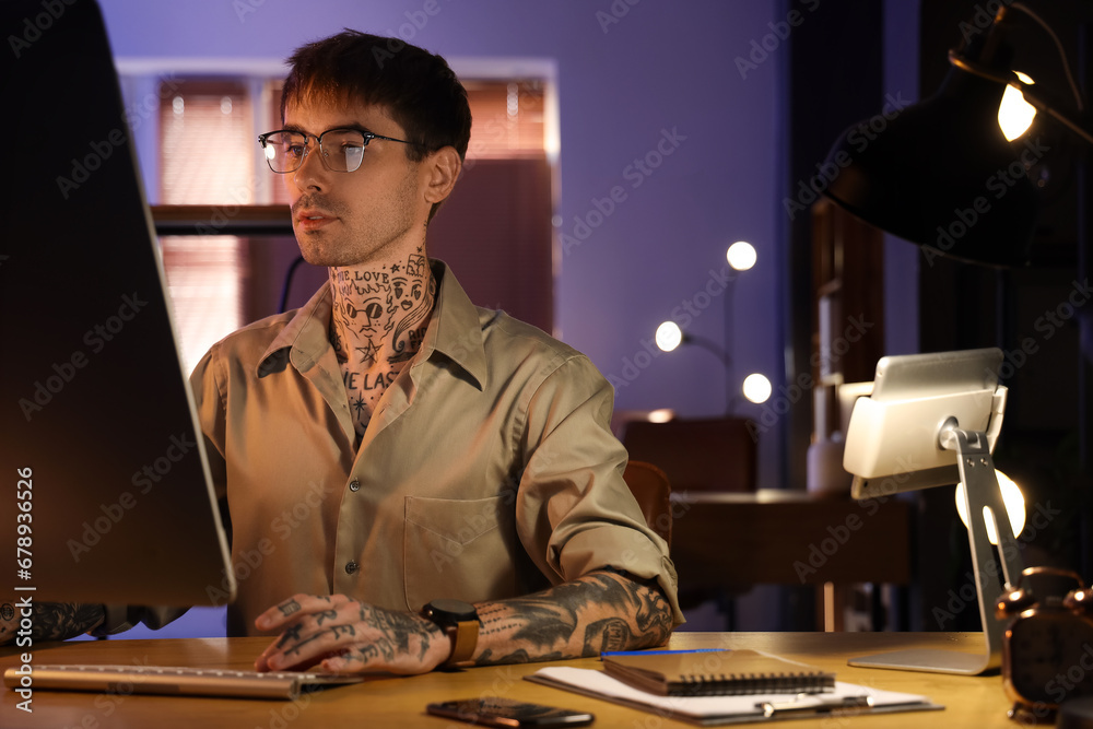 Young tattooed man working with computer in office at night