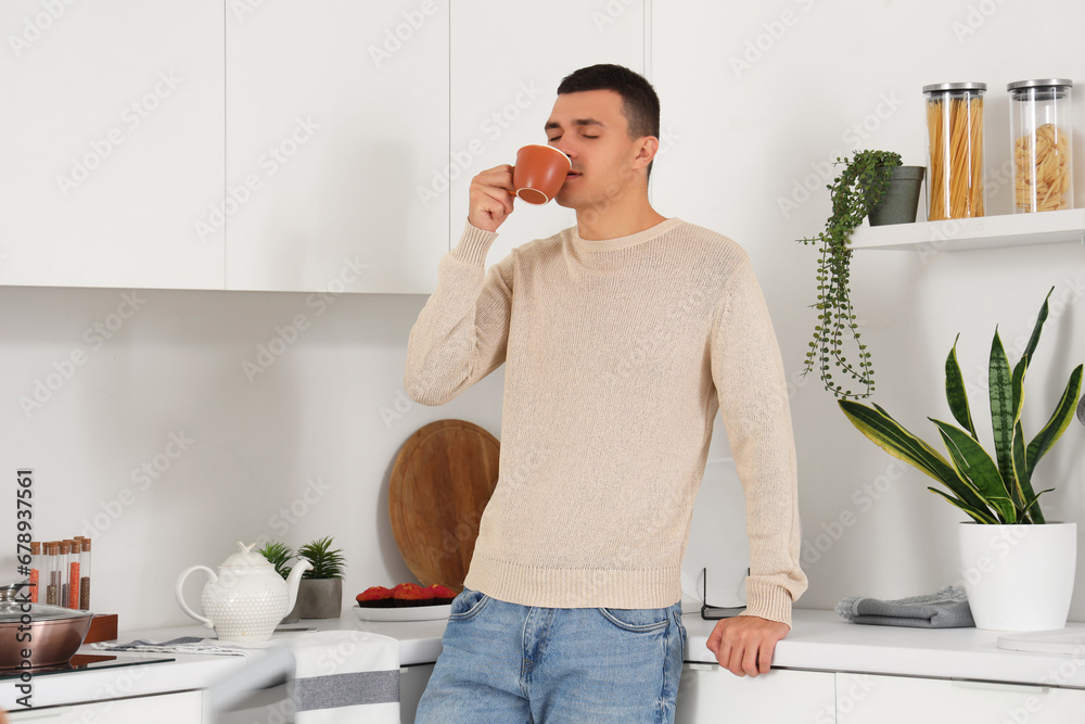 Handsome young man drinking coffee in kitchen at home