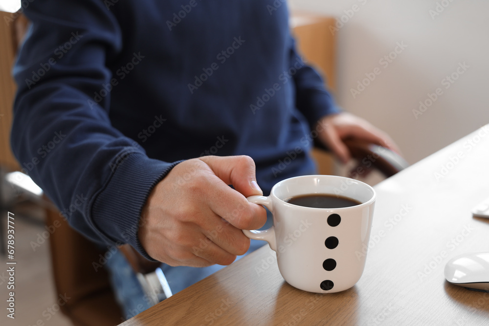 Young man with cup of coffee sitting at his desk in office, closeup