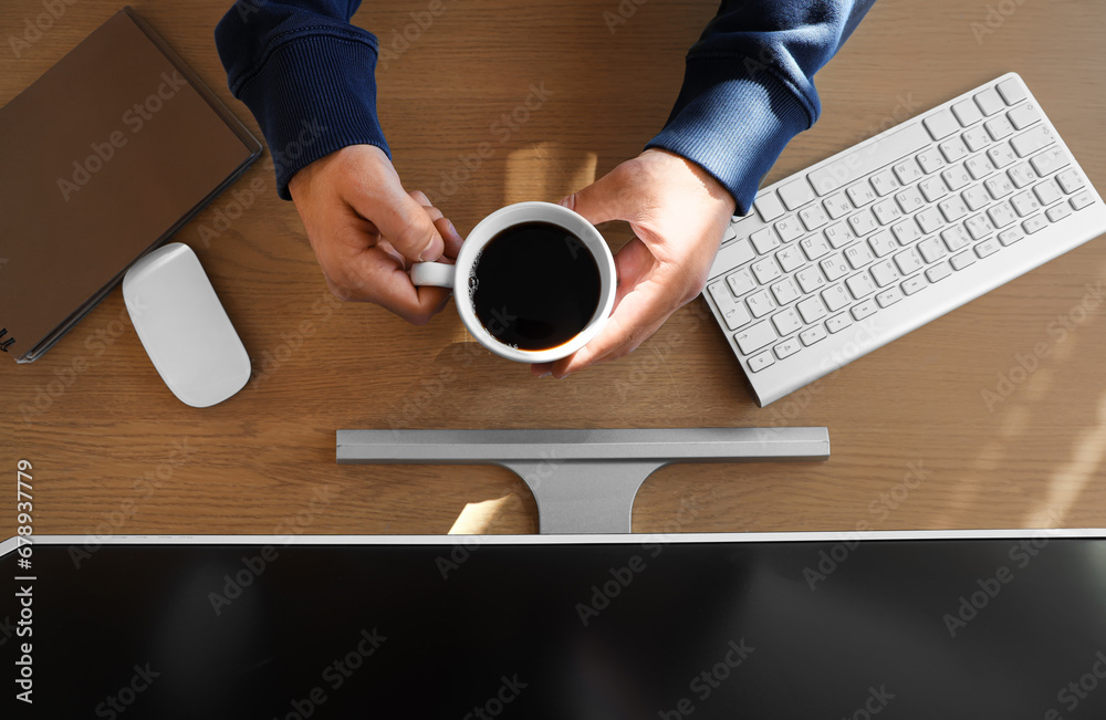 Young man with cup of coffee sitting at his desk in office, top view