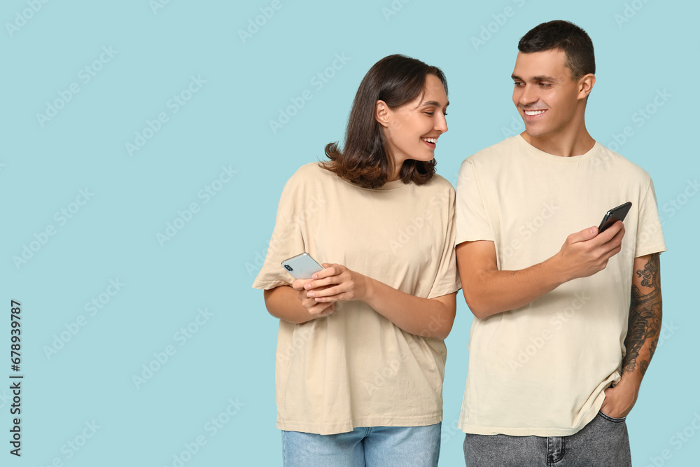 Happy young couple with mobile phones on blue background