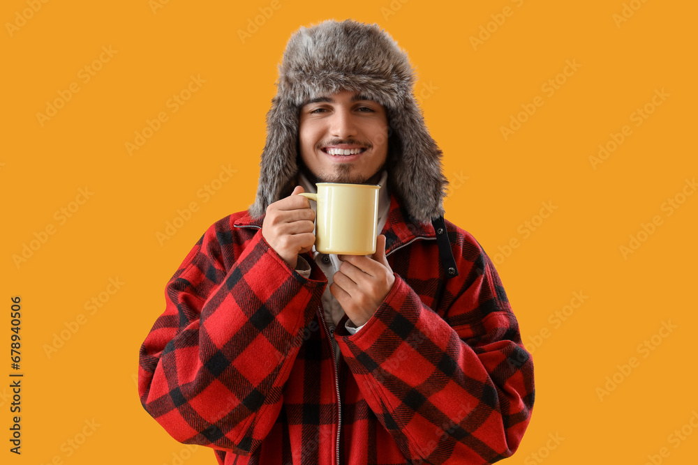 Young man in winter clothes with cup of hot tea on yellow background