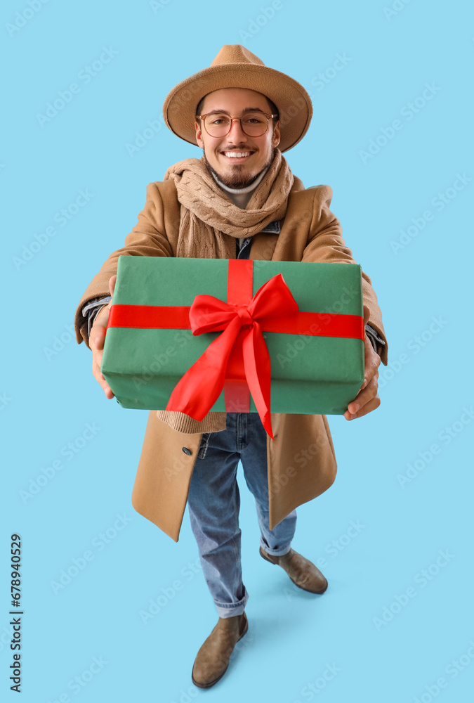 Young man in winter clothes with Christmas gift on blue background