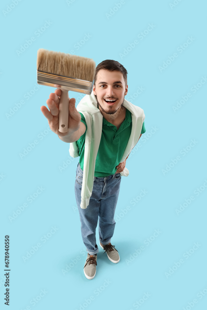 Young man with paint brush on blue background