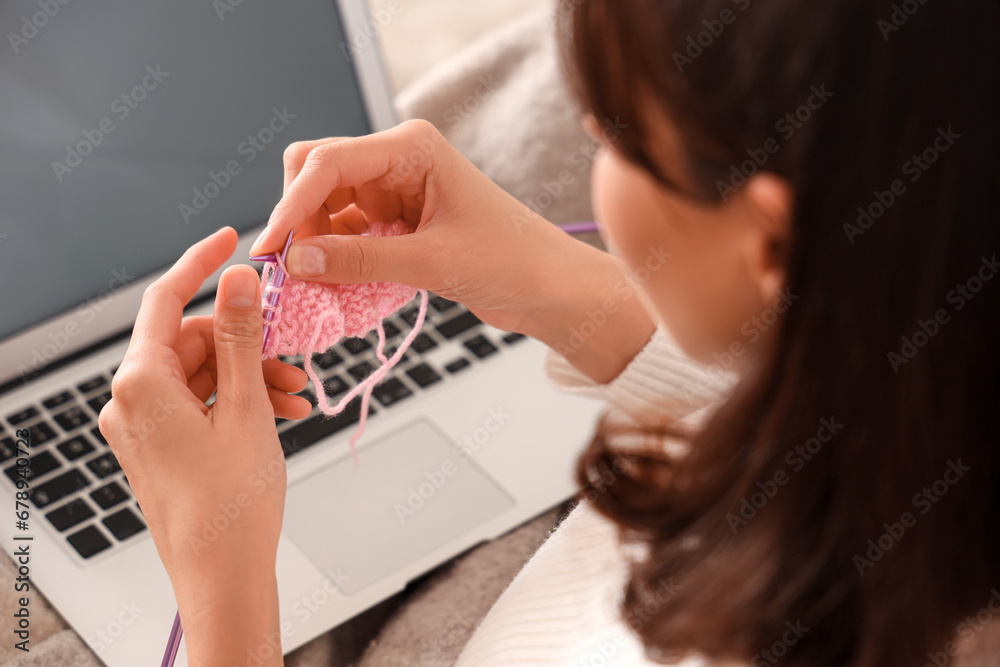 Young woman knitting with needles and laptop at home, closeup