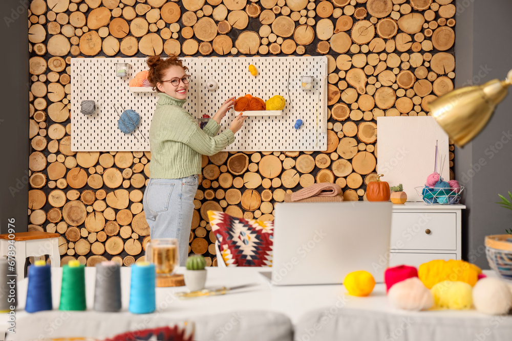 Young woman with knitting yarn on pegboard at home