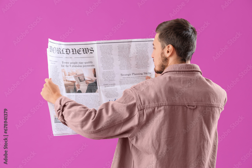 Young man reading newspaper on purple background, back view