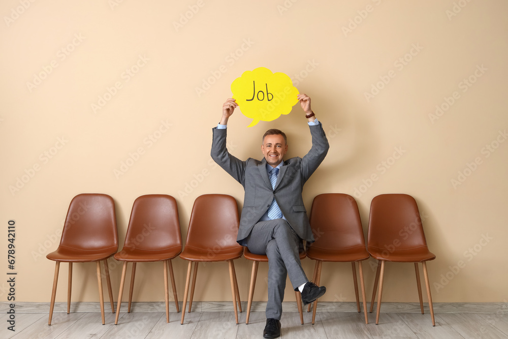 Mature businessman holding speech bubble with word JOB near beige wall