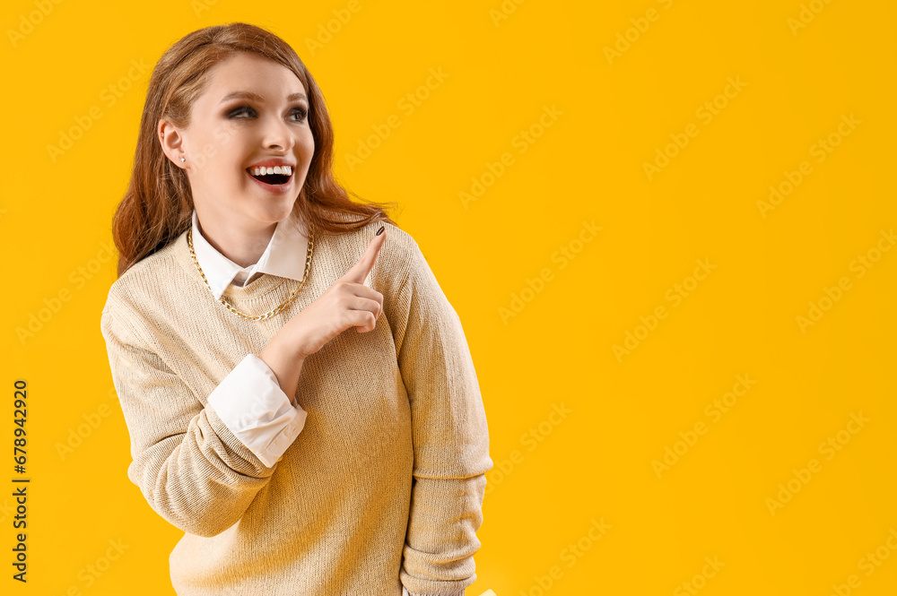 Young gossip woman pointing at something on yellow background