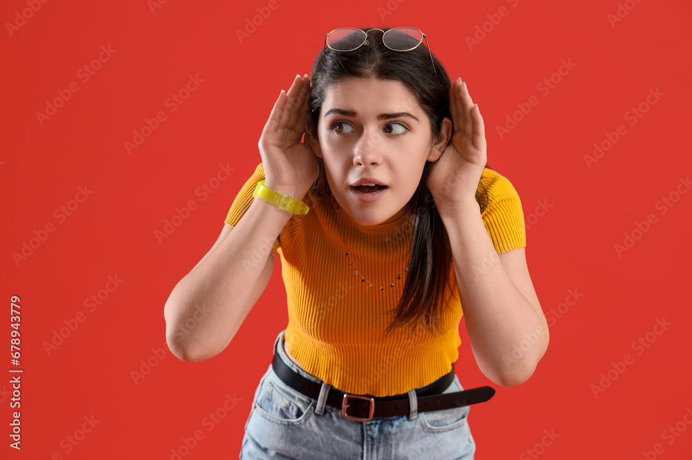 Young gossip woman trying to hear something on red background