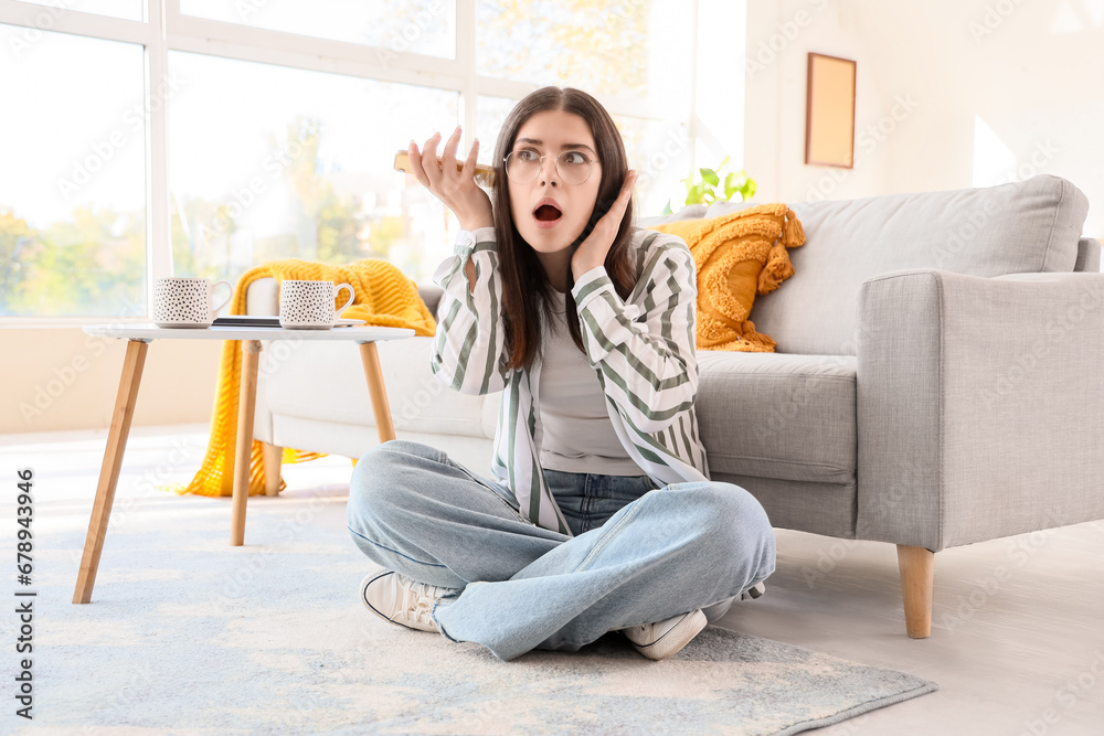 Young gossip woman with mobile phone trying to hear something at home