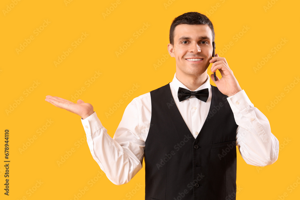 Male waiter with mobile phone showing something on yellow background