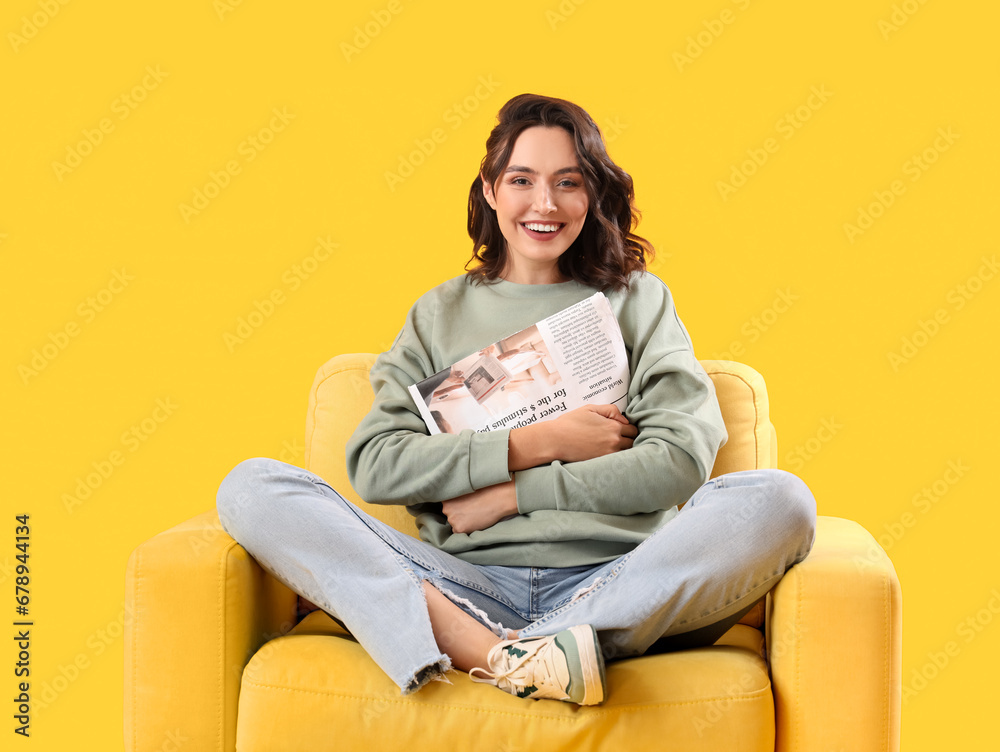 Young woman with newspaper in armchair on yellow background