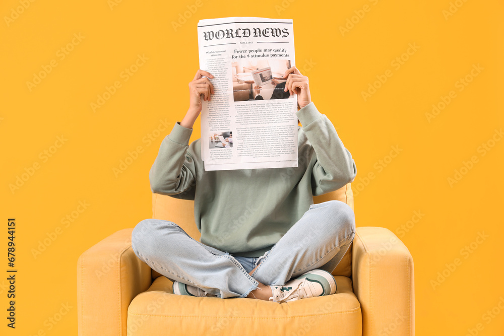 Young woman with newspaper in armchair on yellow background