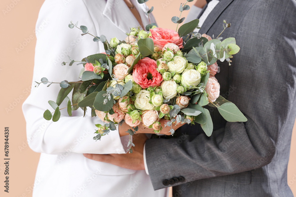 Young wedding couple with bouquet of flowers on beige background, closeup