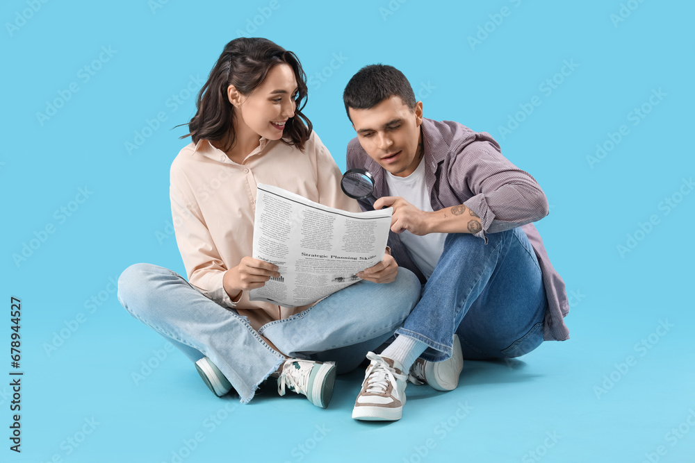 Young couple with newspaper and magnifier on blue background