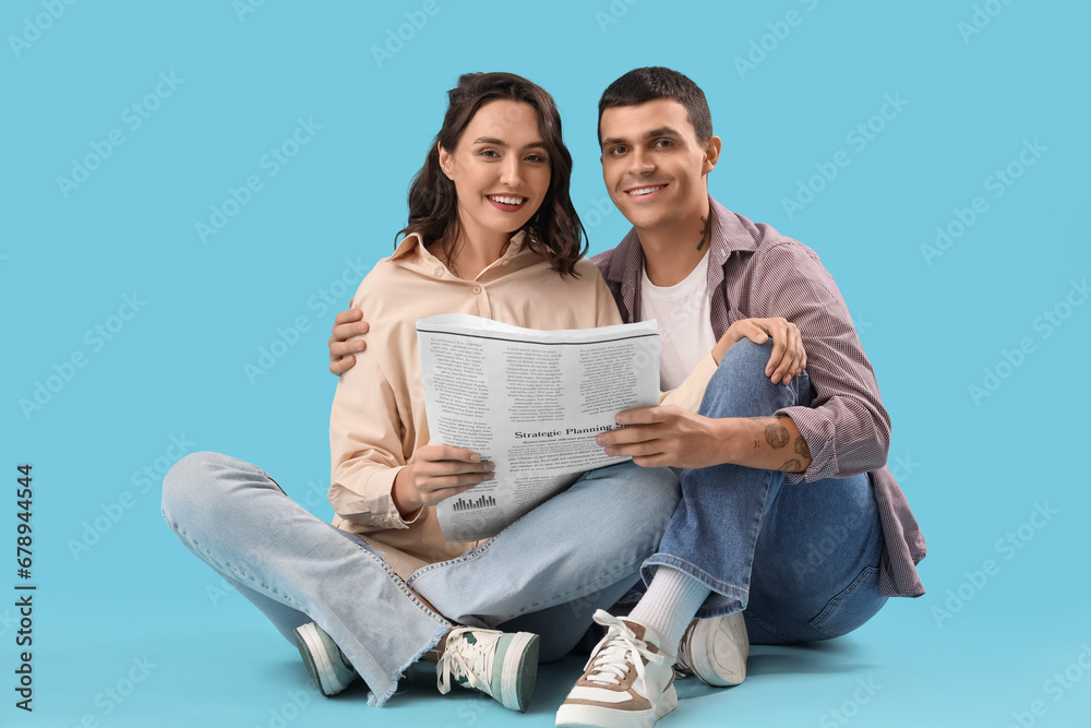 Young couple with newspaper sitting on blue background