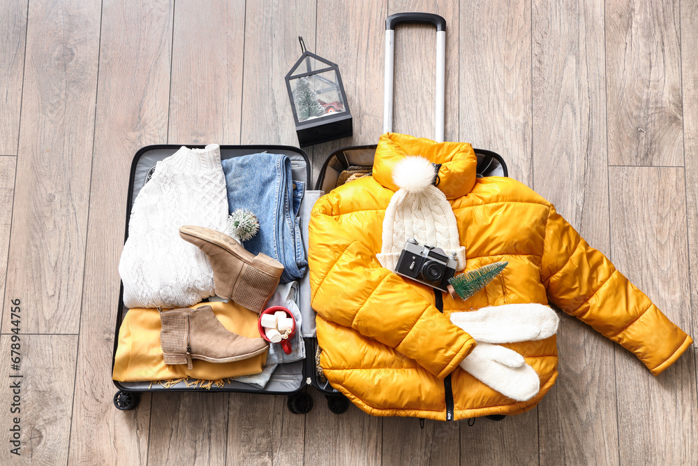 Suitcase with warm clothes, Christmas decorations and cup of cocoa drink on wooden floor