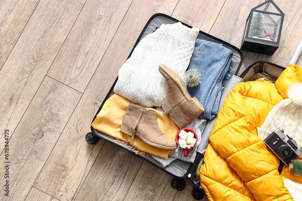 Suitcase with warm clothes, Christmas decorations and cup of cocoa drink on wooden floor