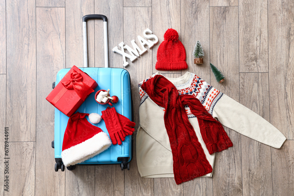 Composition with suitcase, warm clothes and Christmas decorations on wooden floor