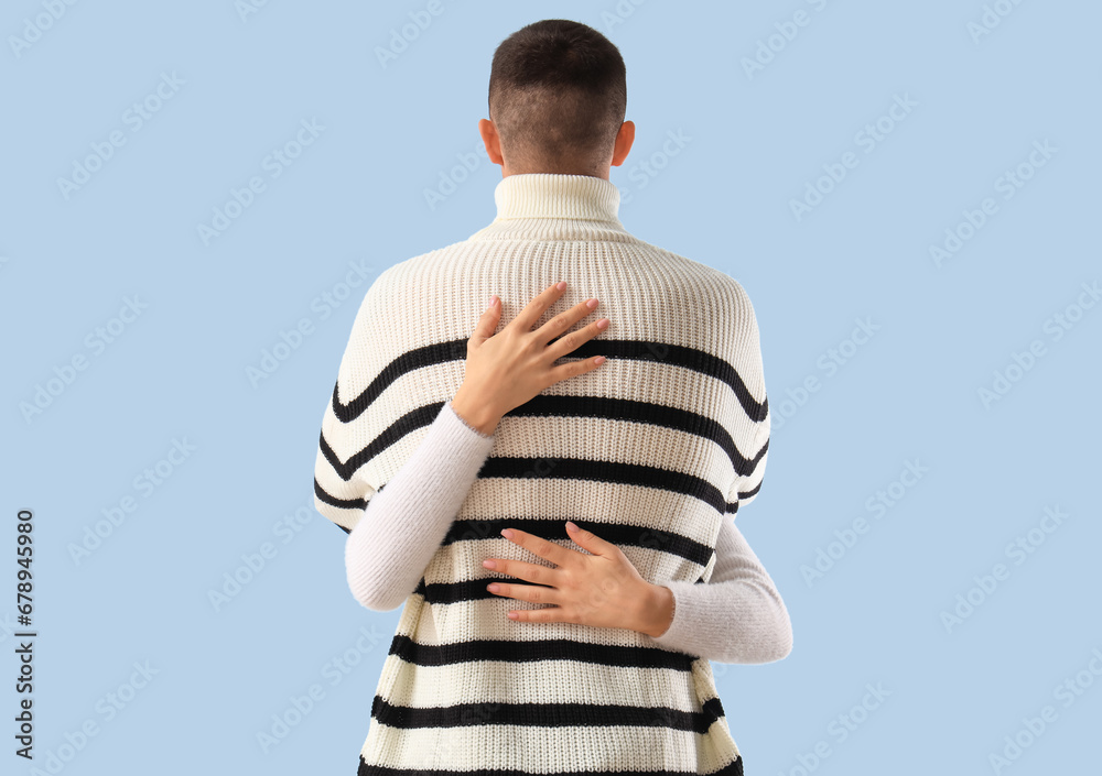 Young couple hugging on blue background, back view