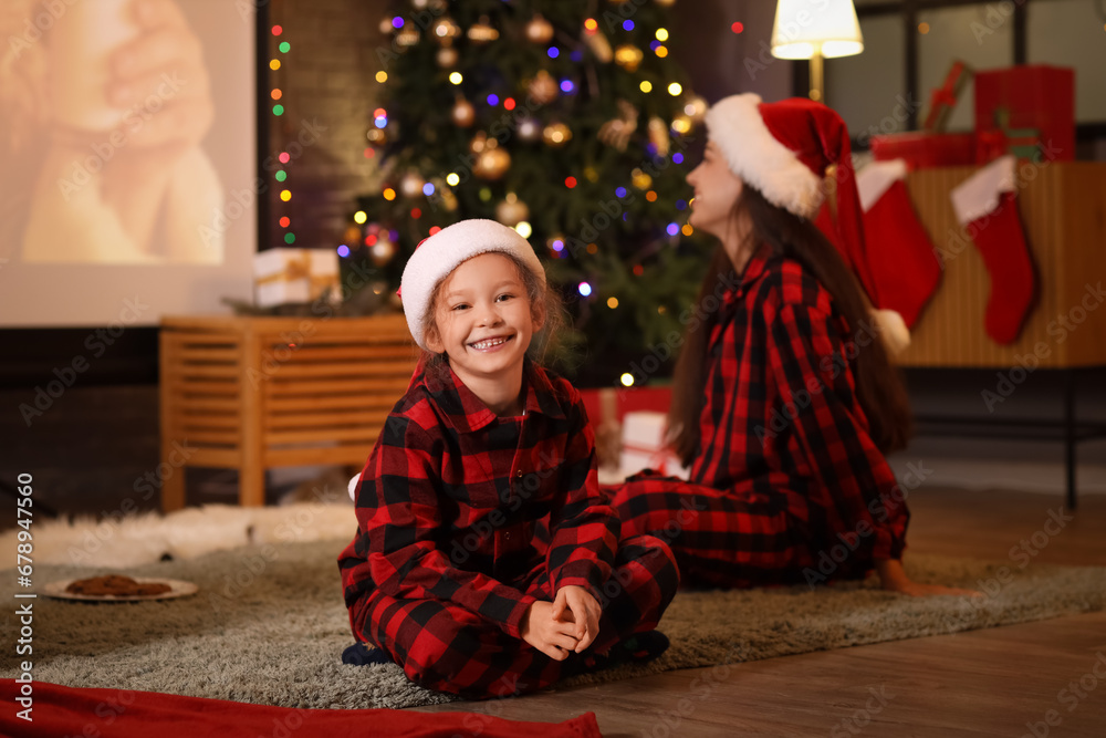 Little girl with her mother watching Christmas movie on projector screen at home