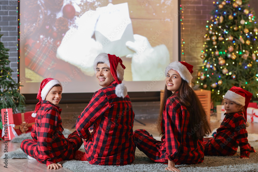 Happy family watching Christmas movie on projector screen at home, back view