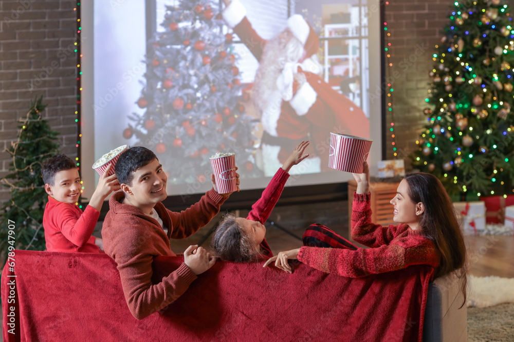 Happy family with popcorn watching Christmas movie on projector screen at home, back view