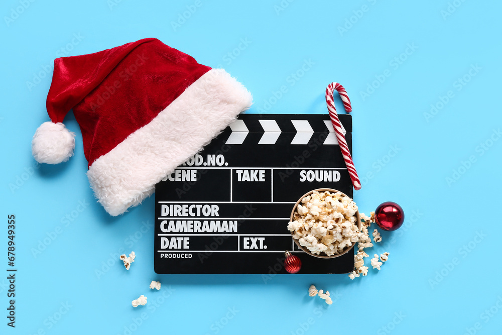 Movie clapper with Santa Claus hat and popcorn on blue background