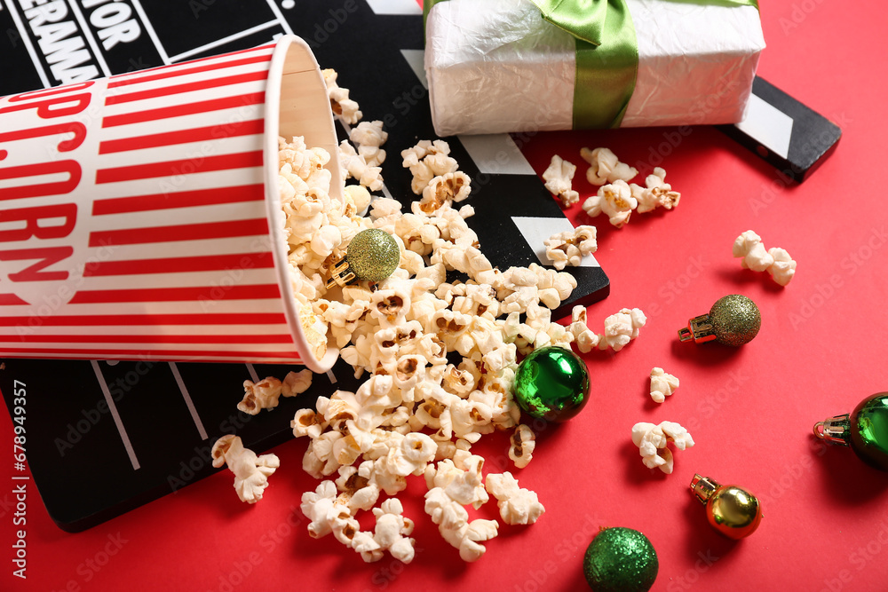 Movie clapper with bucket of popcorn, Christmas balls and gift box on red background