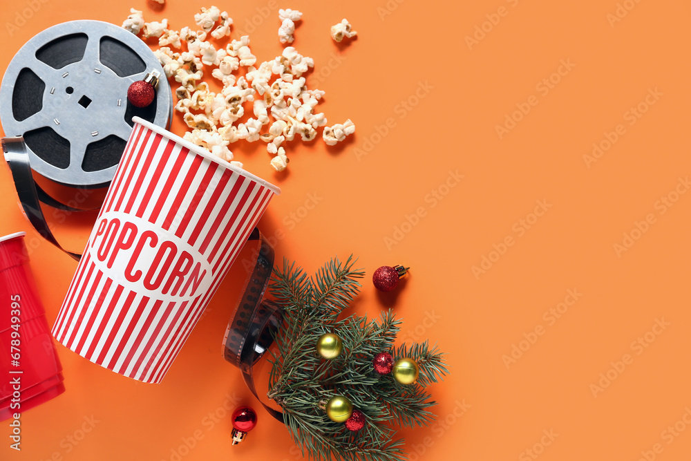 Bucket of popcorn with drink, film reel and Christmas decor on orange background