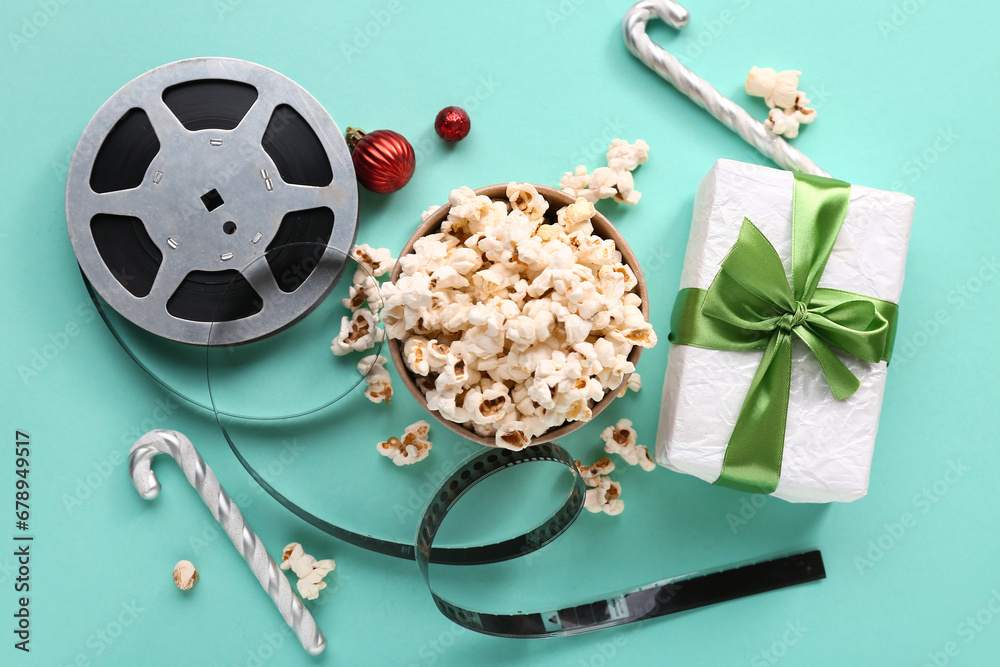 Bucket of popcorn with film reel, candy canes and gift box on turquoise background