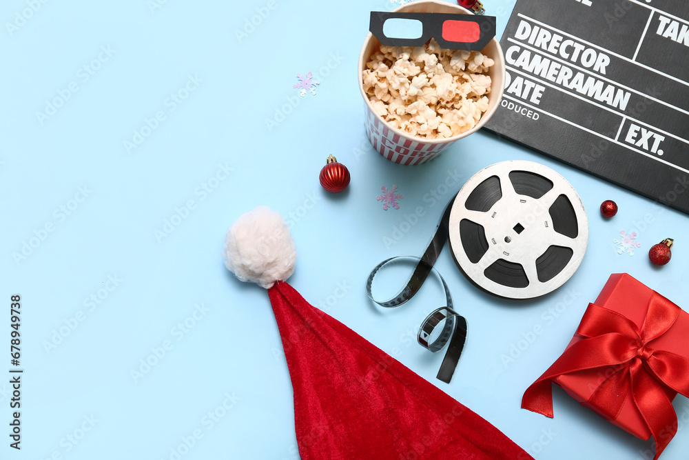 Movie clapper with bucket of popcorn, film reel and Christmas decor on blue background