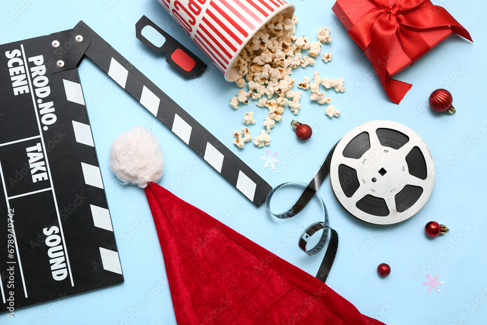 Movie clapper with bucket of popcorn, film reel and Christmas decor on blue background