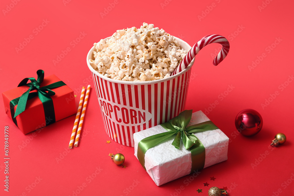 Bucket of popcorn with gifts and Christmas decor on red background