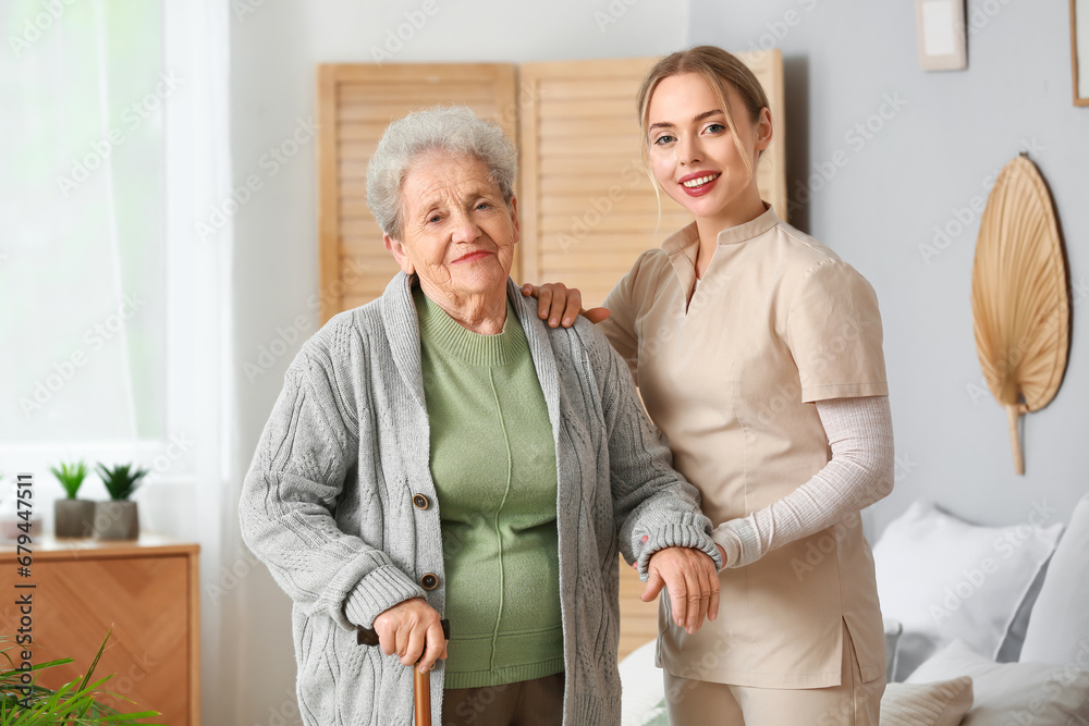 Young caregiver helping senior woman in bedroom