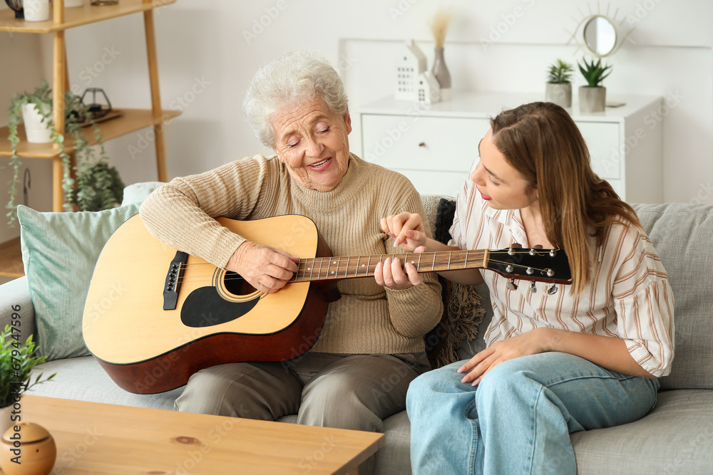 Young woman and her grandmother playing guitar at home