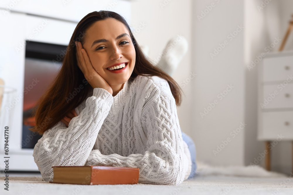 Young woman with book lying near fireplace at home