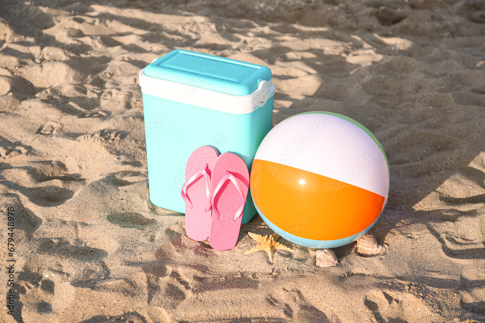 Beach cooler, inflatable ball and flip-flops on sand