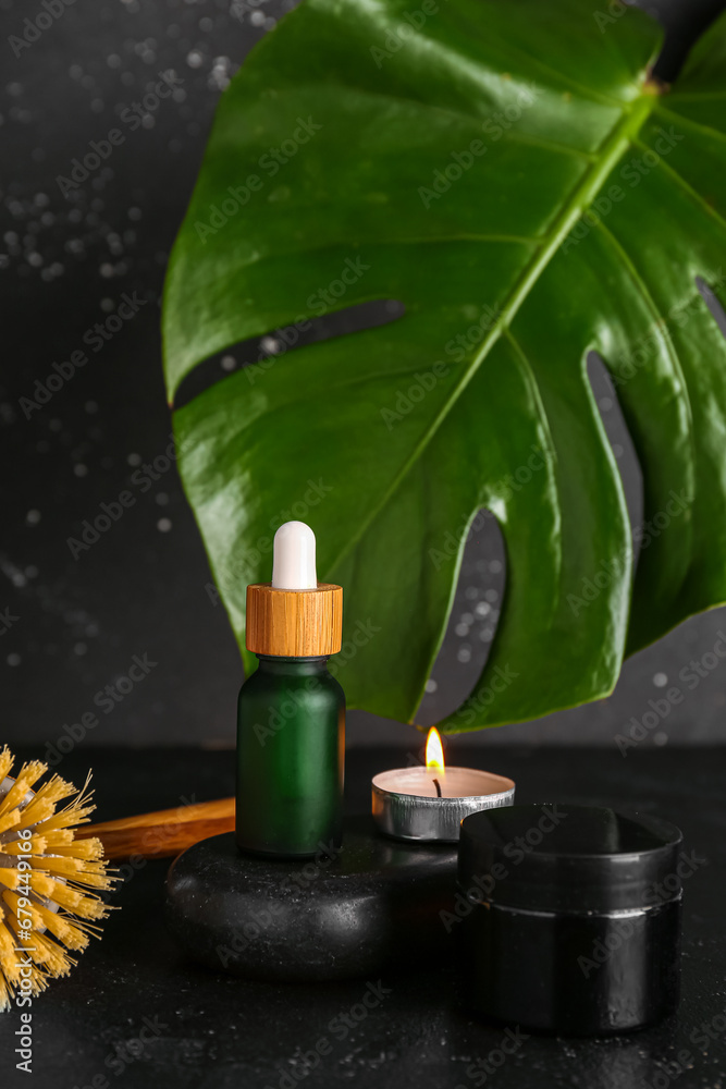 Spa composition with cosmetic products, burning candle and palm leaf on dark background