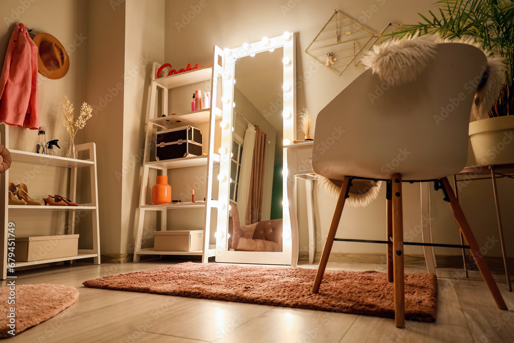 Interior of dark makeup room with glowing mirror and shelf units