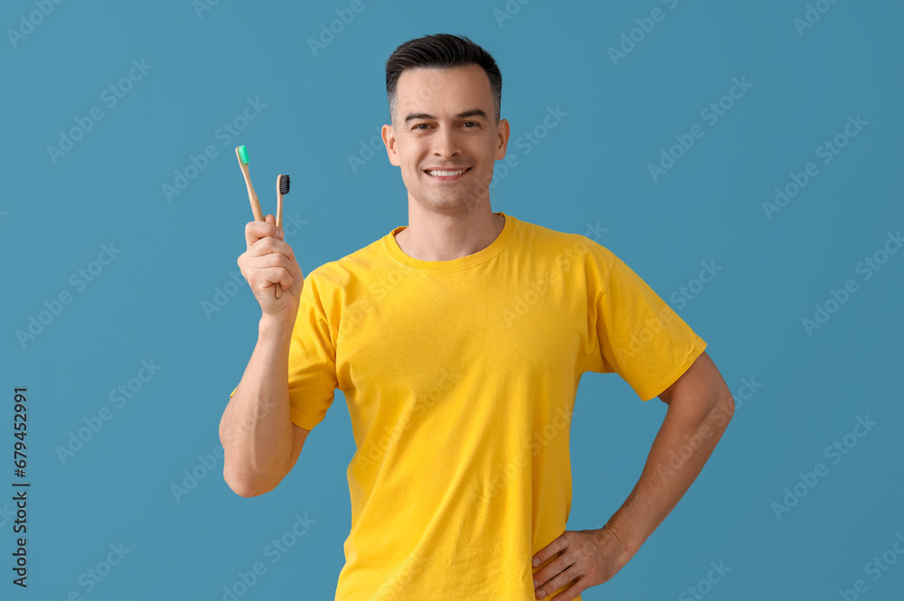 Handsome man with toothbrushes on blue background