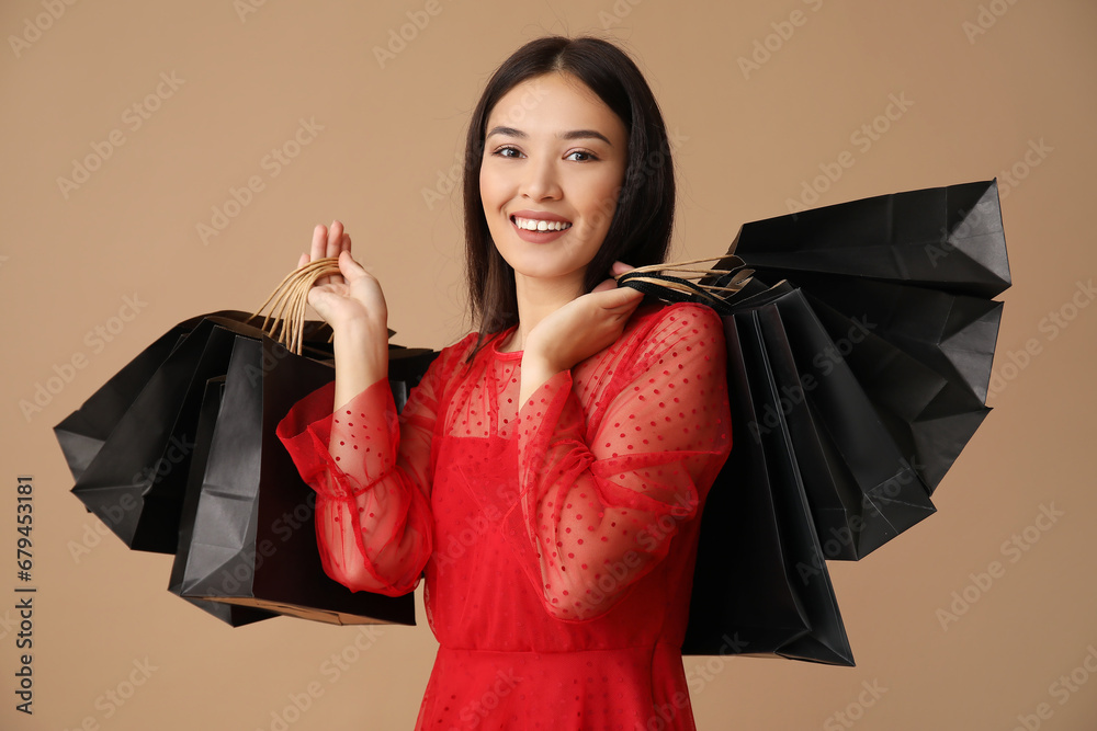 Beautiful young Asian woman with shopping bags on brown background. Black Friday sale