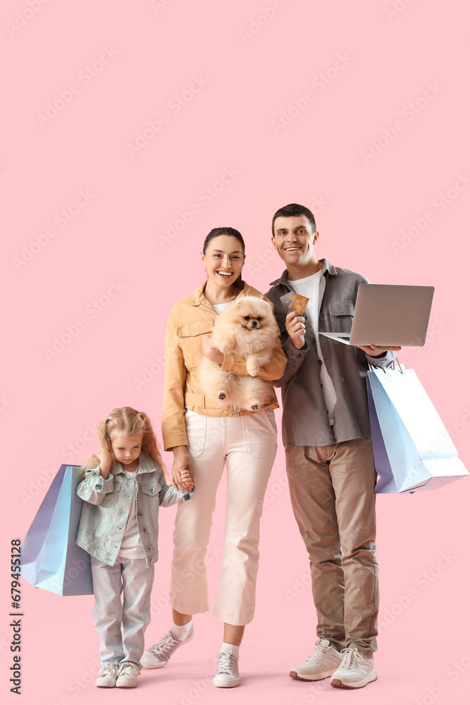 Happy family with laptop and shopping bags on pink background